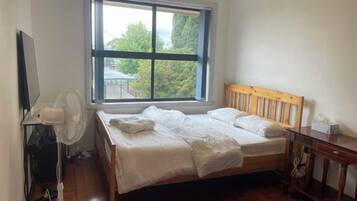 A bedroom with a bed, a wooden headboard, a window, a desk, and a chair.