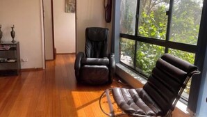 A room with a wooden floor, a black leather chair, a black leather sofa, and a large window with a view of greenery. - 3 Bed room Villa 19 Mins to Melbourne center (Laverton)