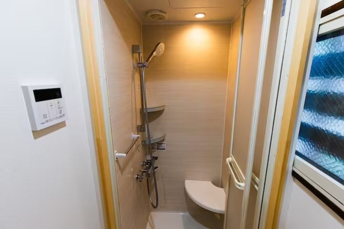 Un baño pequeño con inodoro, ducha y un panel de control en la pared.