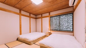 Una habitación con dos camas, una ventana con vistas a árboles, un ventilador de techo y un aire acondicionado de pared.