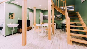 Una habitación con una escalera de madera, una mesa redonda y un lavamanos blanco.