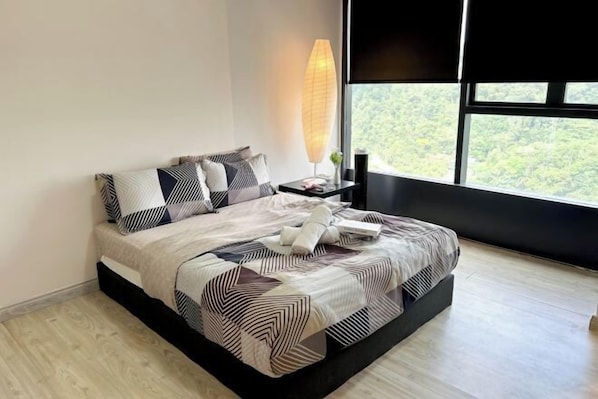 Un dormitorio moderno con una cama grande, ropa de cama con estampado geométrico, una lámpara de noche y vistas a la vegetación a través de un ventanal amplio.