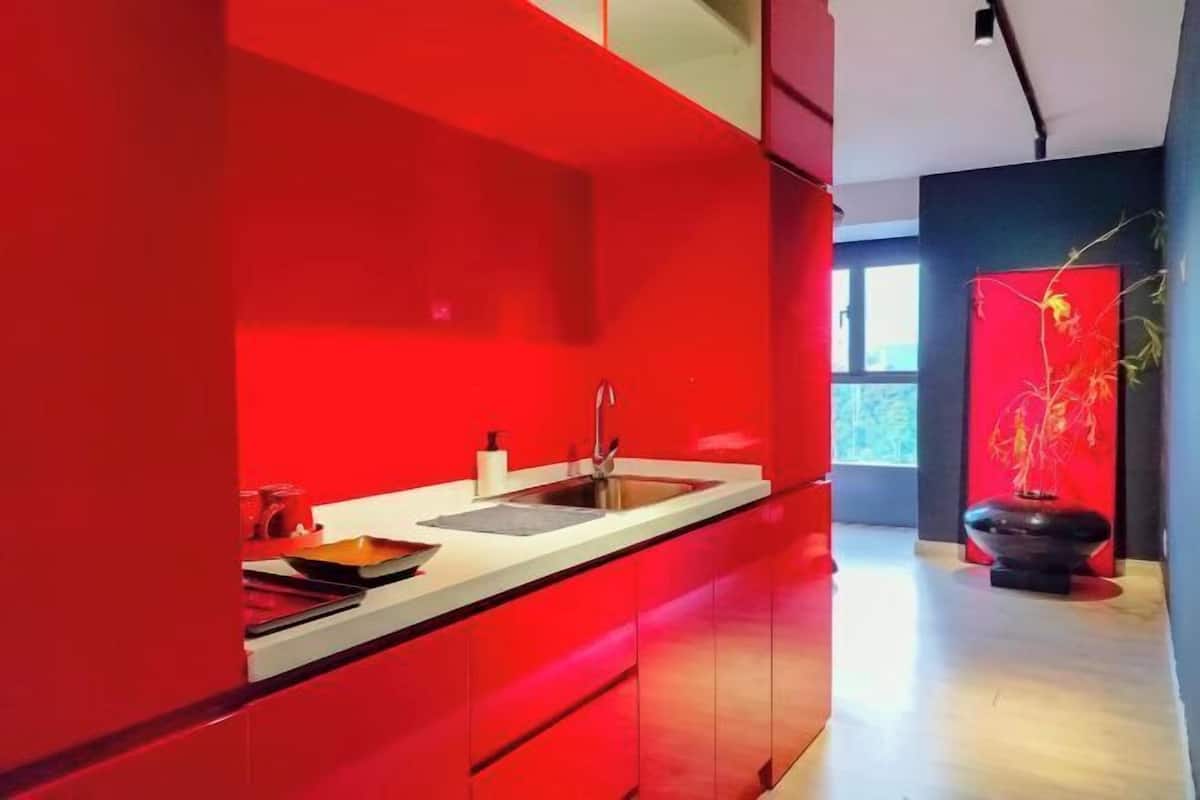 A modern kitchen with red cabinetry, a stainless steel sink, and a black decorative bowl.