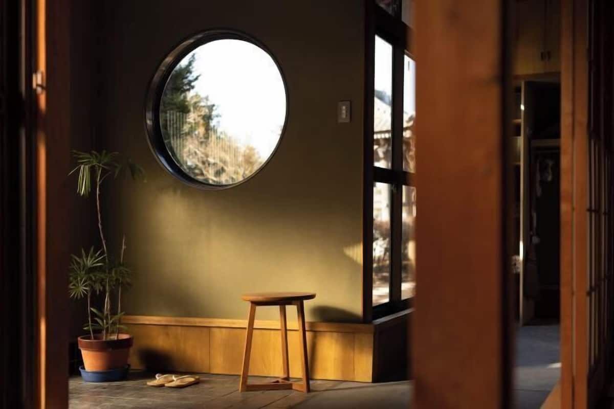 Habitació amb un finestral rodó gran, un tamboret de fusta i una planta en test.