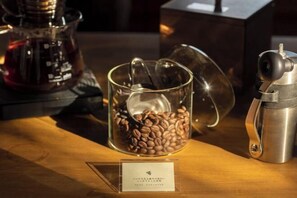 Eine Kaffeemaschine, ein Glasbehälter mit Kaffeebohnen und ein Edelstahl-Wasserhahn auf einer Holztischplatte.
