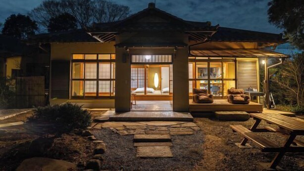A traditional Japanese-style house with a central room featuring a bed, a small porch with seating, and a stone pathway leading to a wooden bench. - TEMPLESTAY ZENSŌ (Chiyoda)
