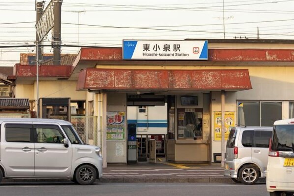 A Higashi-Kozumi Station with a small building, a signboard, and two parked cars. - TEMPLESTAY ZENSŌ (Chiyoda)