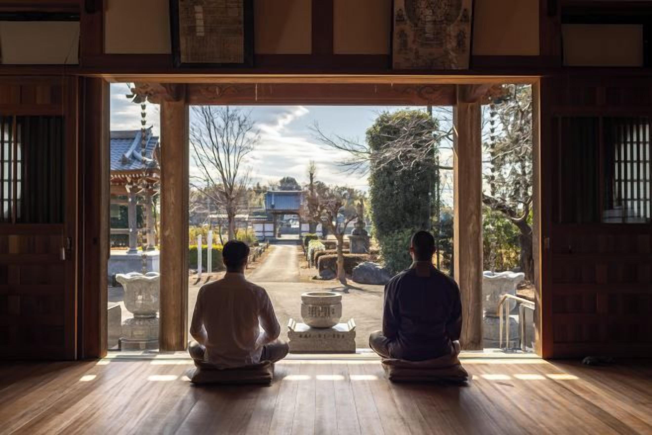 Dos personas sentadas en una habitación con vistas a un edificio tradicional y un sendero exterior.