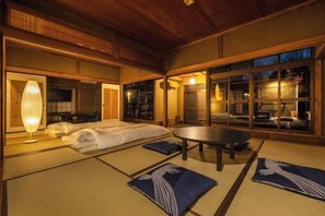 Een traditionele Japanse kamer met tatami vloeren, een bed, een ronde tafel en schuifdeuren met uitzicht.