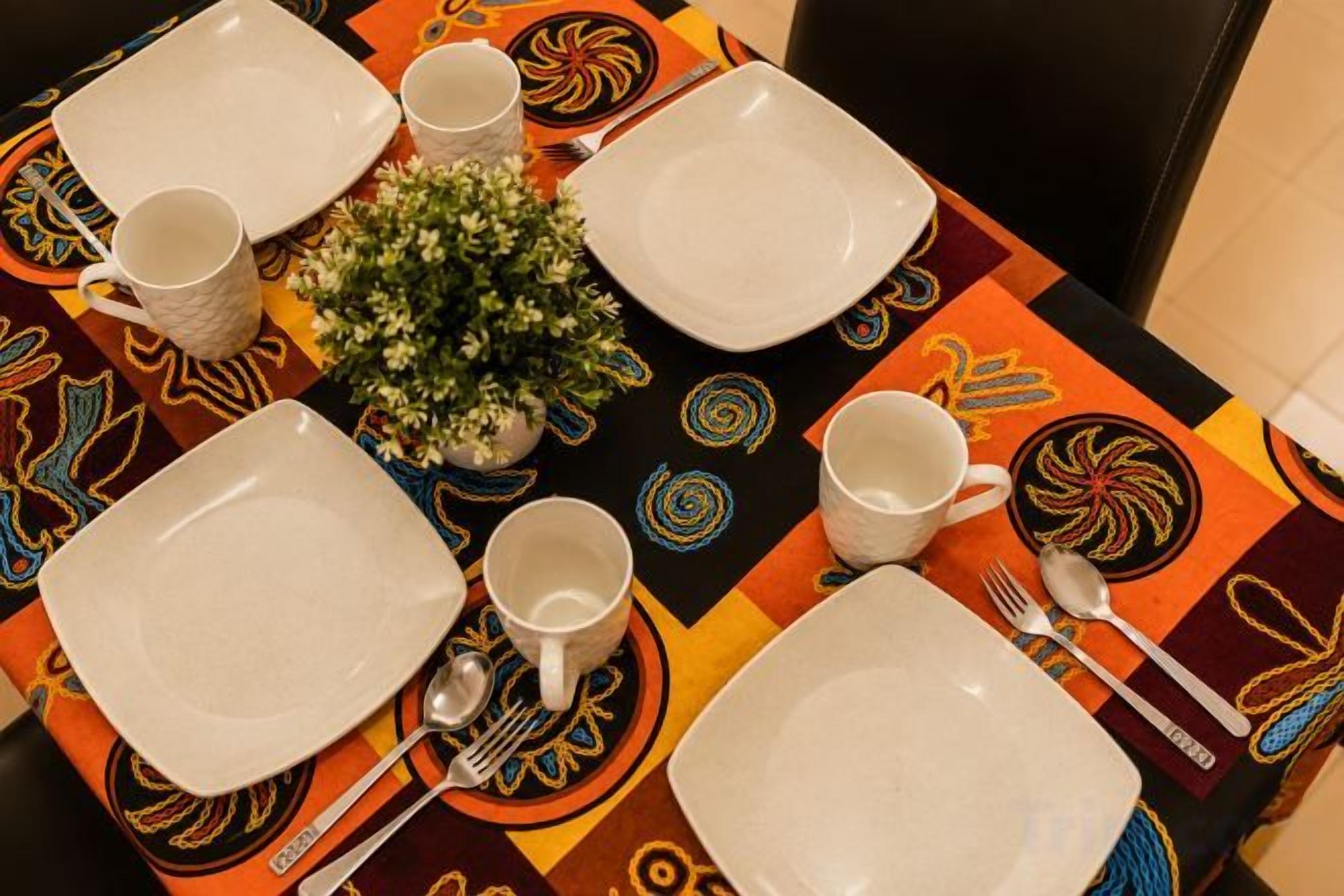 Une table dressée avec des assiettes, des tasses et des couverts, et une petite plante en pot placée au centre.