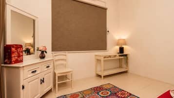 A bedroom with a bed, a bedside table, a chair, a dresser, a mirror, and a window with a blind.