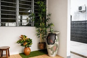 A corner with a window, a potted plant, a vase, and a small stool. - Batu Pahat Sri Jaya Villa 4BR 18pax (Simpang Kanan)