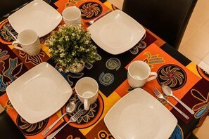 A table set with white plates, cups, and cutlery, centered with a small plant. - Batu Pahat Sri Jaya Villa 4BR 18pax (Simpang Kanan)
