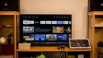 Ein Fernseher auf einem Holzständer, dessen digitale Benutzeroberfläche verschiedene Streaming-Dienste anzeigt.