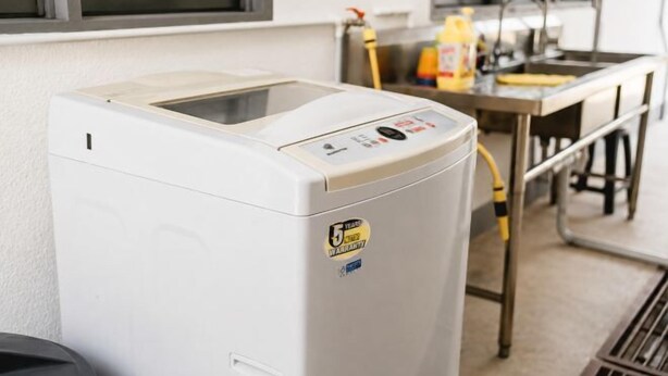 A front-loading washing machine in a laundry area with a sink and a window in the background.