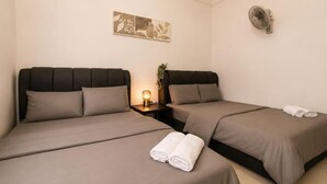 A hotel room with two beds, a bedside table with a lamp, and a wall-mounted fan.