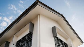 A building corner with a white facade, a sloped roof, and two windows with shutters.