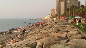 A rocky beach with people sunbathing and swimming, a row of umbrellas, and tall buildings in the background. - Sea side apartment in "Batumi View" (Batumi)