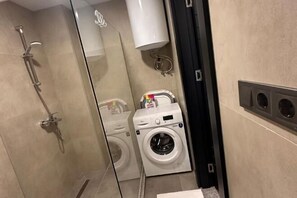 A bathroom with a glass shower enclosure, a washing machine, and a towel rack. - Sea side apartment in "Batumi View" (Batumi)