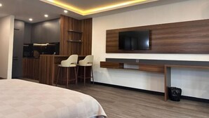 A modern hotel room with a bed, a TV mounted on the wall, a small kitchen area, and a seating area with chairs. - Sea side apartment in "Batumi View" (Batumi)