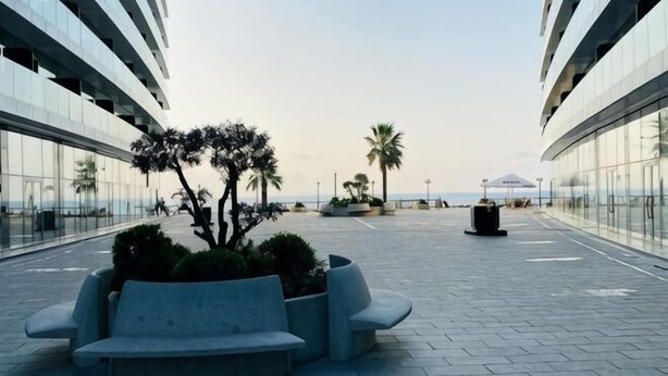 A modern outdoor area with a seating bench, a planter with shrubs, and a trash bin. - Sea side apartment in "Batumi View" (Batumi)