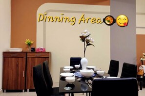 Un coin repas avec une table dressée pour quatre personnes, un vase de fleurs et un mur sur lequel on peut lire le texte « Coin repas » accompagné d’émojis.