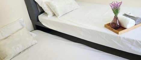 Una cama doble con ropa de cama blanca, un cabecero gris, un jarrón con flores y una bandeja con una almohada y una toalla.