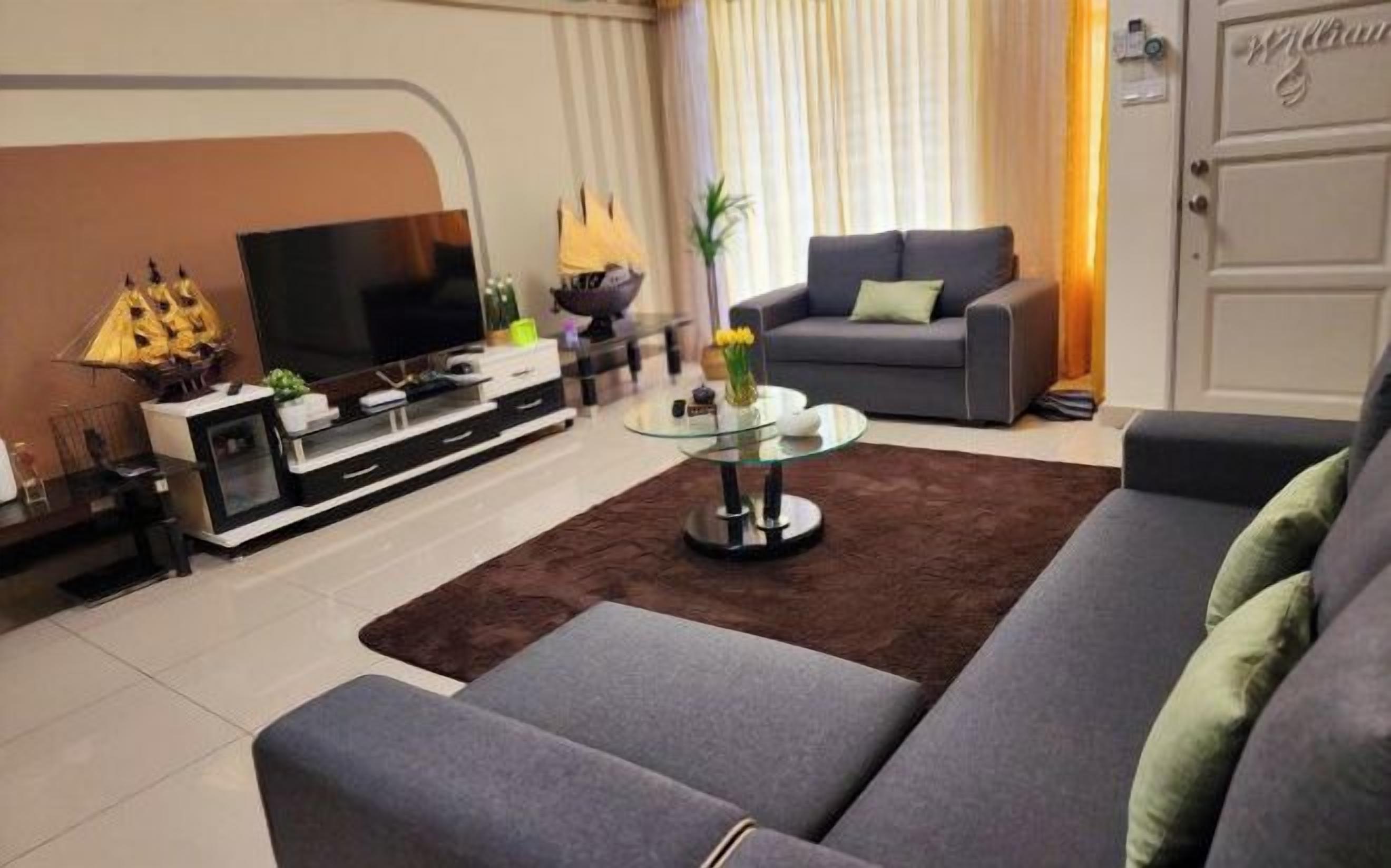 A modern living room with a grey sofa, a glass coffee table, and a flat-screen TV.
