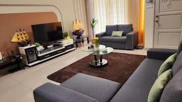 A modern living room with a grey sofa, a glass coffee table, and a flat-screen TV.