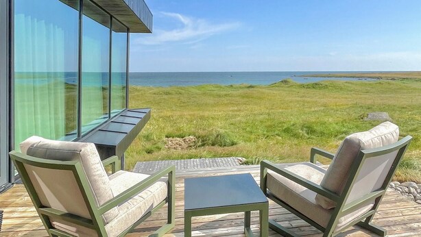 Um terraço com duas cadeiras e uma mesa, com vista para um campo gramado e o mar.