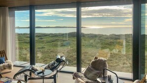 Quarto com janelas amplas que oferecem vista para um lago e terras distantes. Há uma cadeira com uma manta e um ursinho de pelúcia.