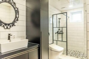 Une salle de bain avec un lavabo blanc, un miroir doté d’un cadre orné et un espace douche avec une porte en verre.
