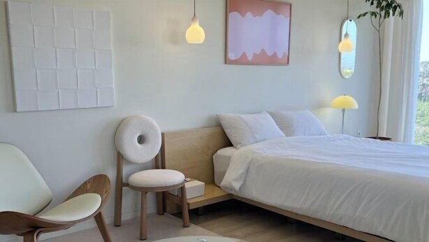 A modern bedroom with a bed, a chair, a bedside table, and a wall-mounted artwork. - Mon Monde Aewol (Jeju)