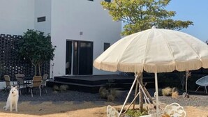 A modern outdoor patio with a white umbrella, seating, and a dog. - Mon Monde Aewol (Jeju)