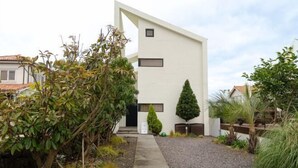 A modern building with a white facade, a gravel pathway, and various plants. - Mon Monde Aewol (Jeju)