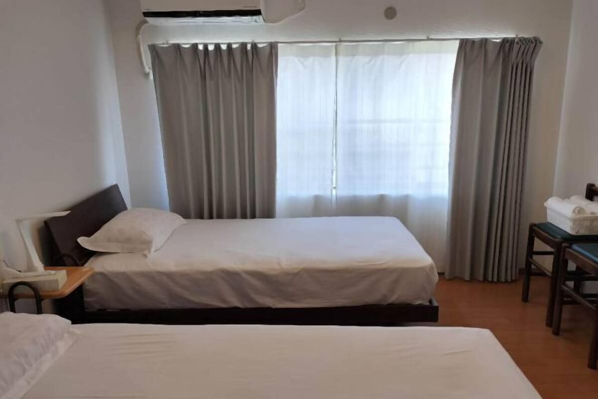 A hotel room with a bed, a desk, an air conditioning unit, and a window with curtains.