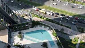 Vista aérea de un hotel con piscina, sillas de descanso y una carretera con vehículos.