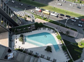 An aerial view of a hotel with a swimming pool, lounge chairs, and a road with vehicles.