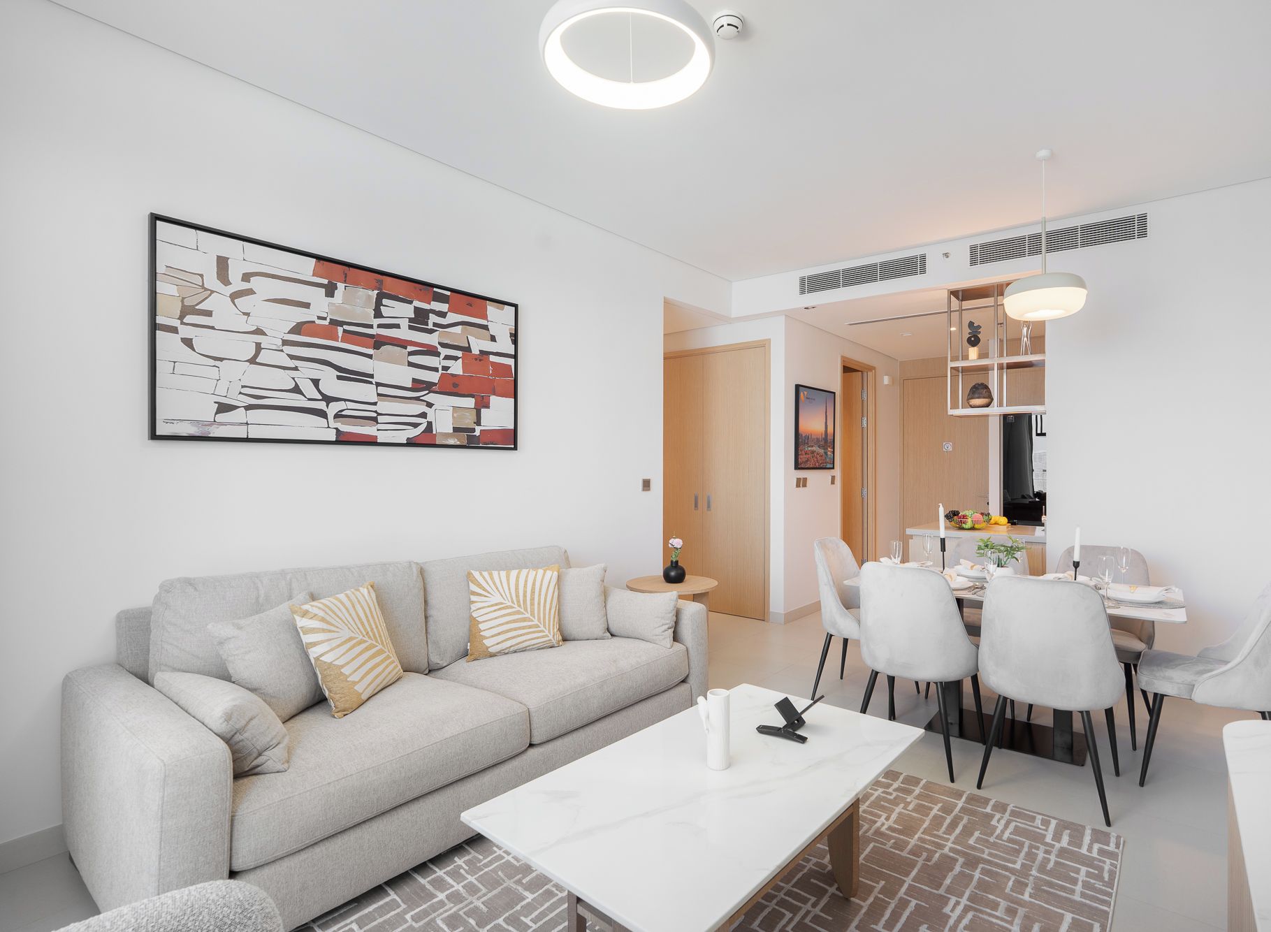A modern living room with a sofa, coffee table, and dining area with chairs and a table set for a meal.