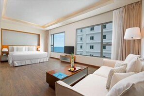 Une chambre d’hôtel comprenant un lit, un canapé, une table basse, une télévision et une grande fenêtre donnant sur des immeubles.