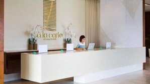 A reception desk with a modern design, featuring a logo and name of the establishment. There are two laptops on the desk, and a person is seated behind it. - A La Carte Beachfront Lovers Bliss Retreat Studio (Da Nang)