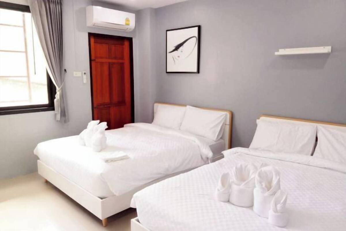 A hotel room with two beds, a wooden door, a framed picture on the wall, and a white air conditioning unit.