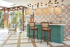 Eine Bar mit einem türkisfarbenen Tresen, Korbstühlen und hängenden Rattanlampen.