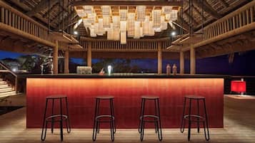 An outdoor bar area with a wooden deck, a central bar counter, and three stools.