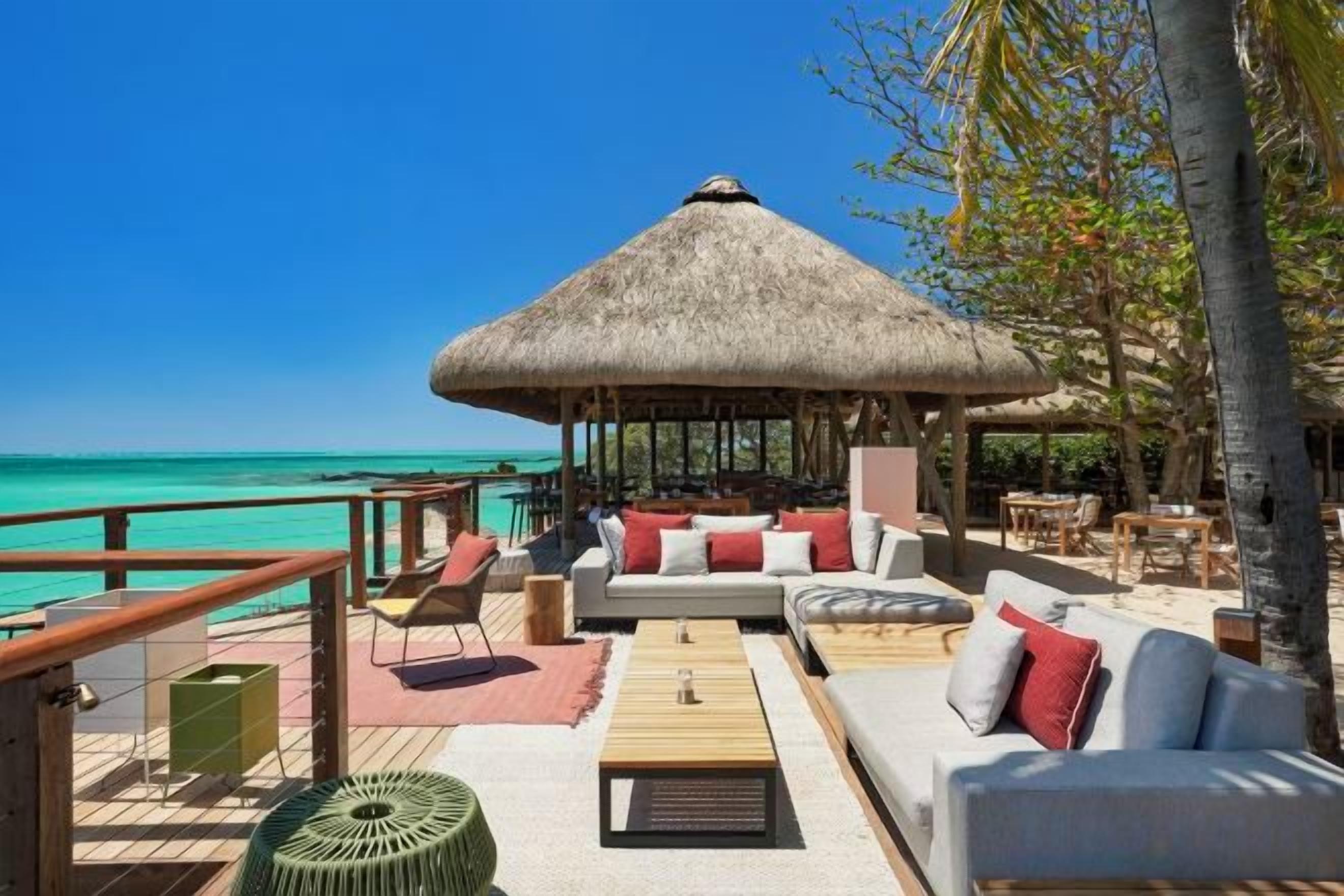 Un salón frente a la playa con techo de paja, asientos al aire libre y vista al océano.