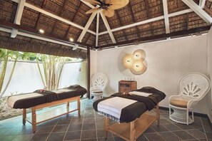 Ein Zimmer mit zwei Betten, einem Deckenventilator, einer Wandleuchte und einem weißen Stuhl.