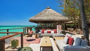 Un espace de détente extérieur doté d’un toit de chaume, d’une terrasse en bois et de différents coins salon offrant une vue sur une mer turquoise.