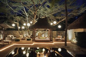 Un espace de détente extérieur aménagé pour la nuit, comprenant un belvédère, des sièges et un bassin décoratif.