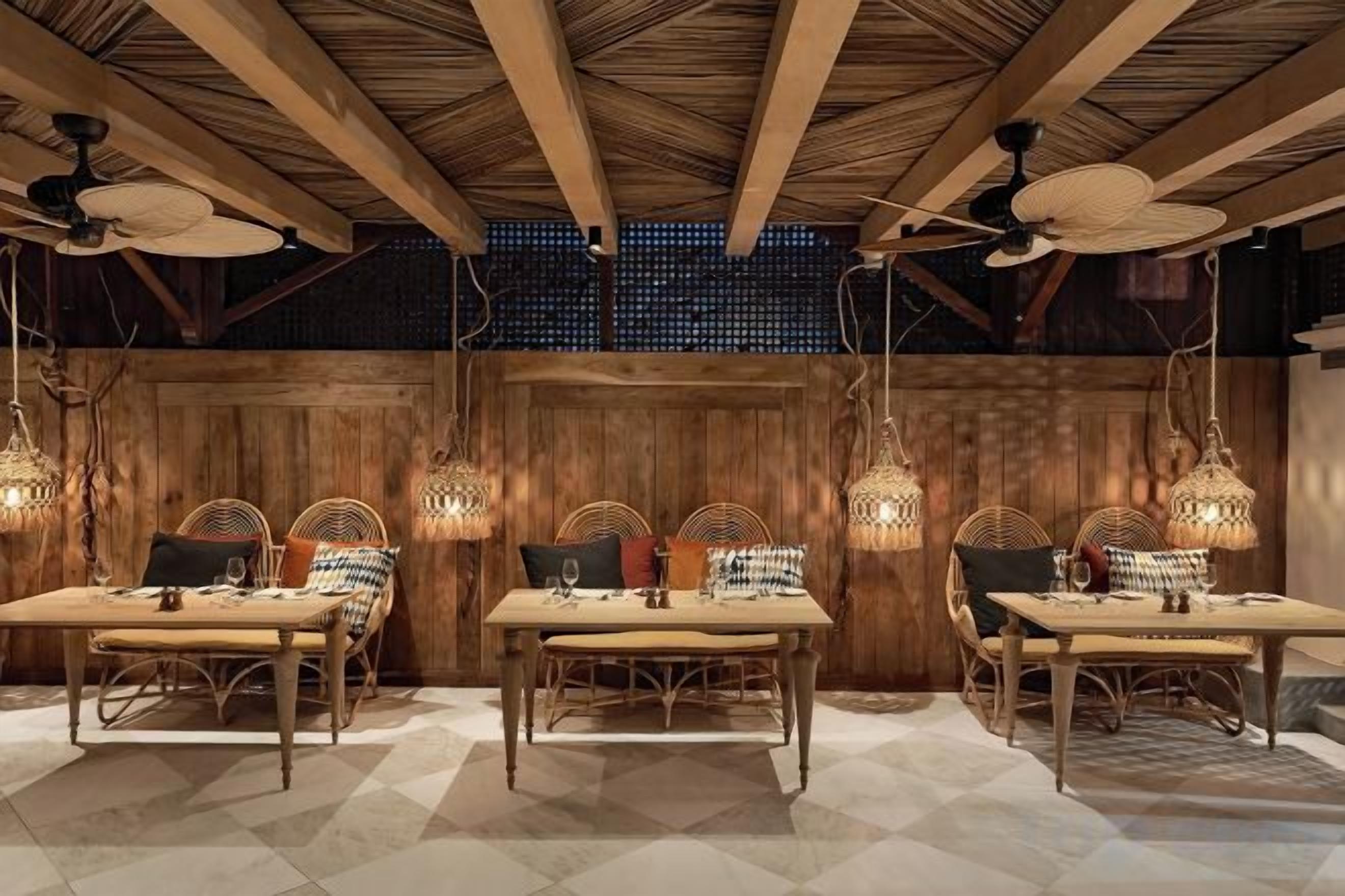 Un comedor con mesas y sillas de madera, luces colgantes y techo de madera.
