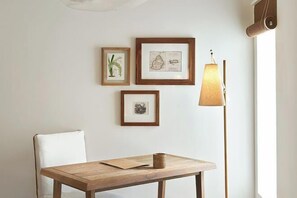 Une pièce au décor minimaliste, avec une table en bois, une chaise blanche et trois œuvres d’art encadrées accrochées au mur.